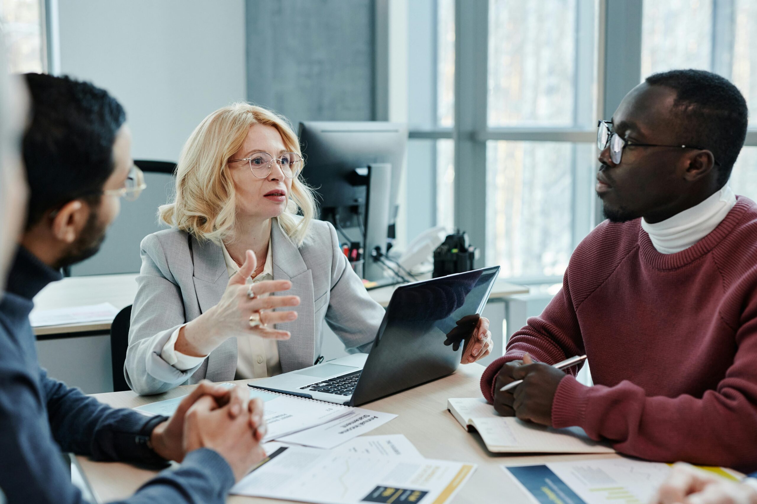 Business professionals discussing strategy around a table with a laptop in an office setting.
